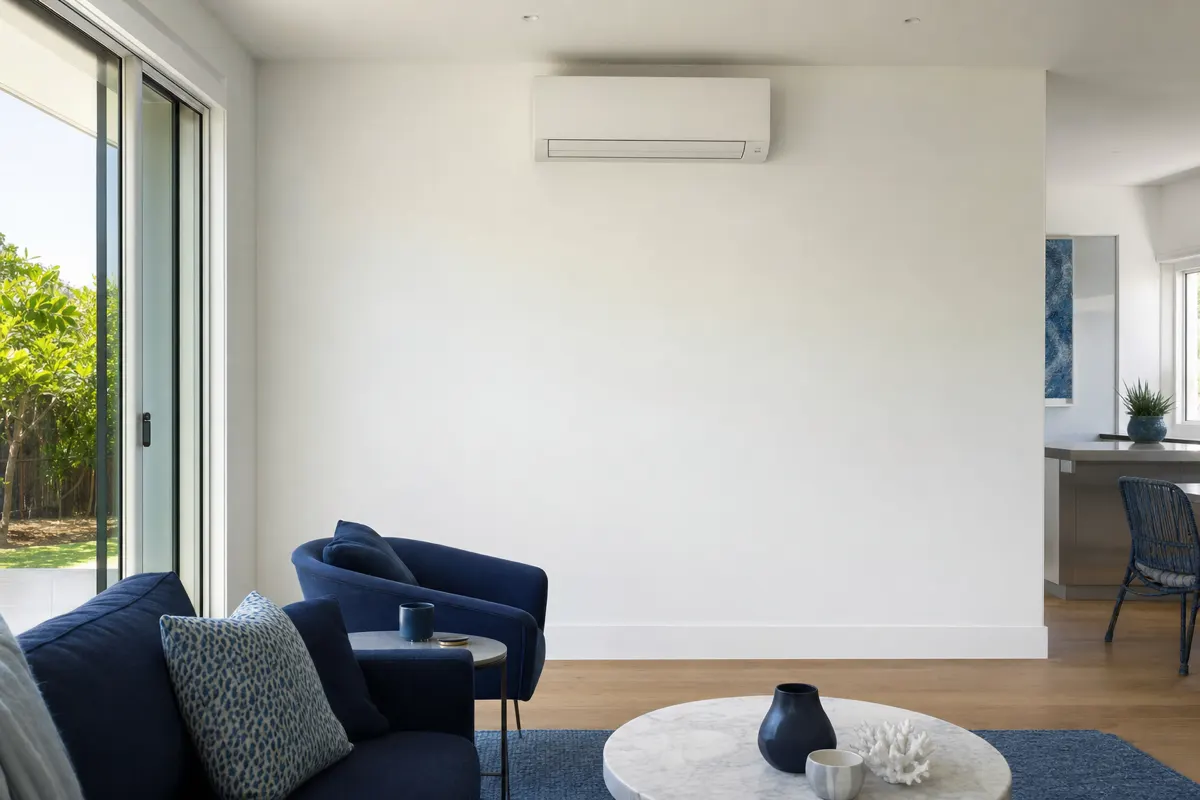 Wall-hung split system head high on a plain wall in a bright modern living room